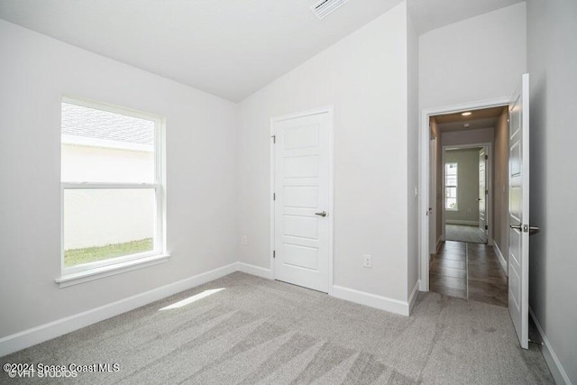 unfurnished bedroom with light carpet, multiple windows, and lofted ceiling