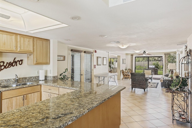 kitchen with ceiling fan, sink, light tile floors, dark stone counters, and light brown cabinetry