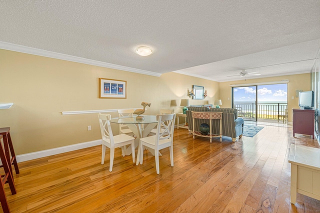 dining area featuring a textured ceiling, ceiling fan, light wood-type flooring, and crown molding