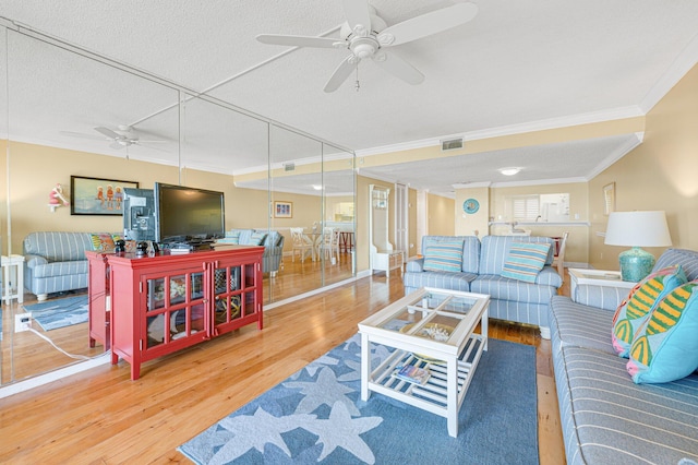 living room featuring a textured ceiling, ornamental molding, ceiling fan, and light wood-type flooring