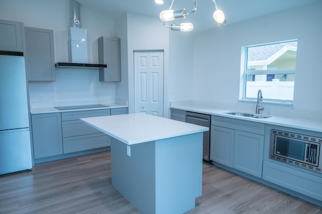 kitchen featuring sink, pendant lighting, stainless steel appliances, wall chimney range hood, and light wood-type flooring