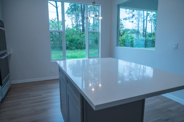 kitchen with an inviting chandelier, hardwood / wood-style floors, hanging light fixtures, and light stone counters