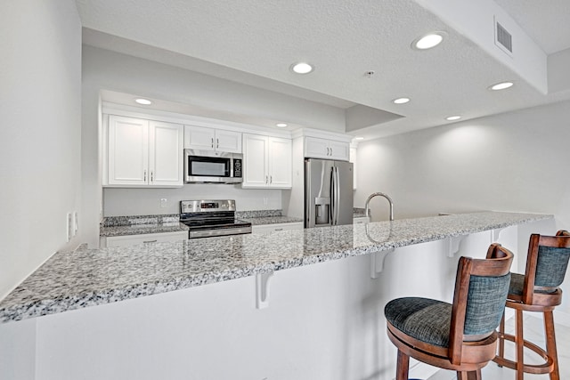 kitchen featuring white cabinets, appliances with stainless steel finishes, light stone countertops, and a kitchen bar