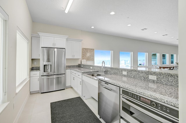 kitchen featuring light tile flooring, sink, stainless steel appliances, white cabinets, and light stone counters