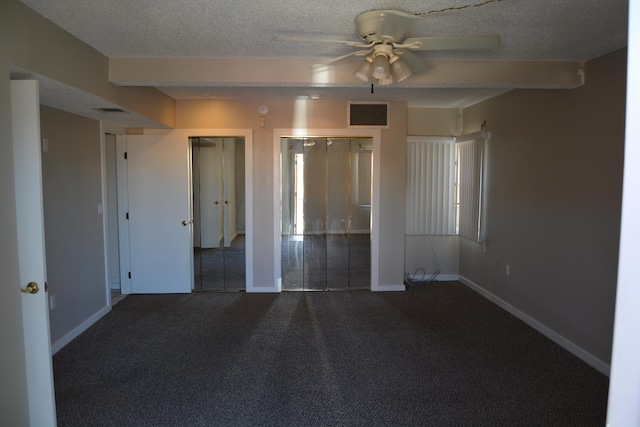 unfurnished bedroom featuring two closets, a textured ceiling, ceiling fan, and dark carpet