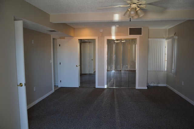 unfurnished bedroom with a textured ceiling, multiple closets, dark colored carpet, and ceiling fan