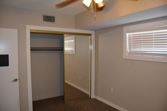 unfurnished bedroom with dark carpet, a closet, ceiling fan, and a textured ceiling