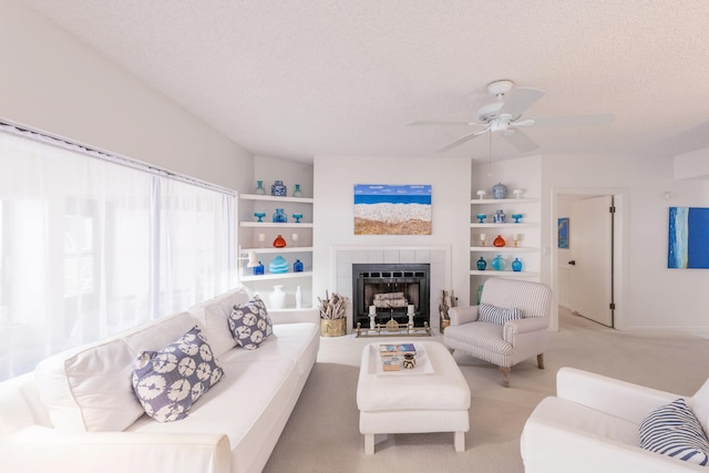 living room with ceiling fan, built in features, light carpet, a textured ceiling, and a tile fireplace