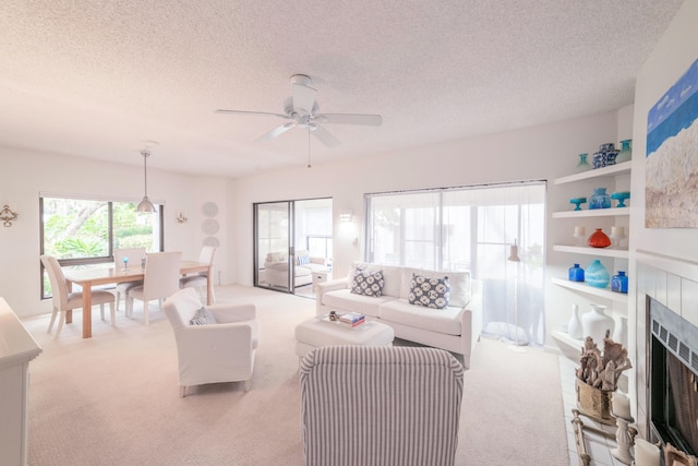 carpeted living room featuring a textured ceiling, ceiling fan, and a fireplace