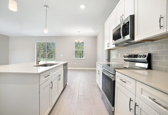 kitchen with sink, stainless steel appliances, an island with sink, decorative light fixtures, and white cabinets