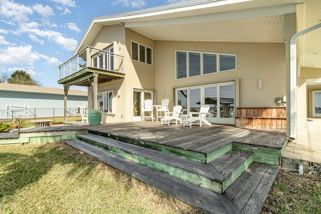 rear view of house with a lawn, a deck, and a balcony