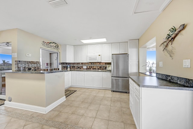 kitchen with tasteful backsplash, kitchen peninsula, stainless steel fridge, and white cabinets