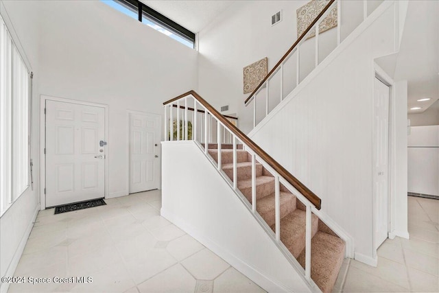 stairs featuring tile patterned flooring, a healthy amount of sunlight, and a high ceiling