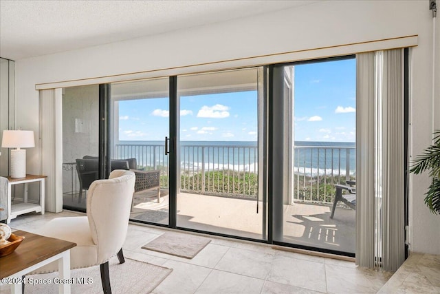 doorway featuring a view of the beach, light tile patterned floors, a textured ceiling, and a water view