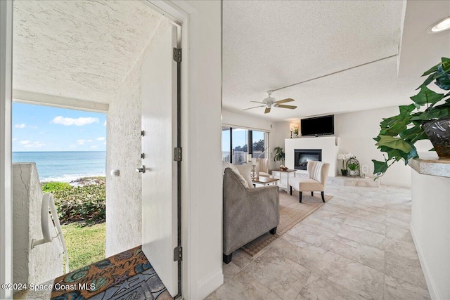 living room with ceiling fan, a water view, a view of the beach, and a textured ceiling