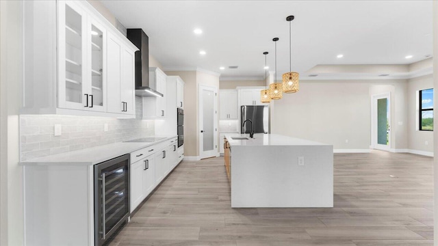 kitchen featuring beverage cooler, light hardwood / wood-style flooring, backsplash, black appliances, and an island with sink