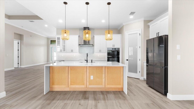 kitchen with wall chimney exhaust hood, pendant lighting, light wood-type flooring, black appliances, and backsplash