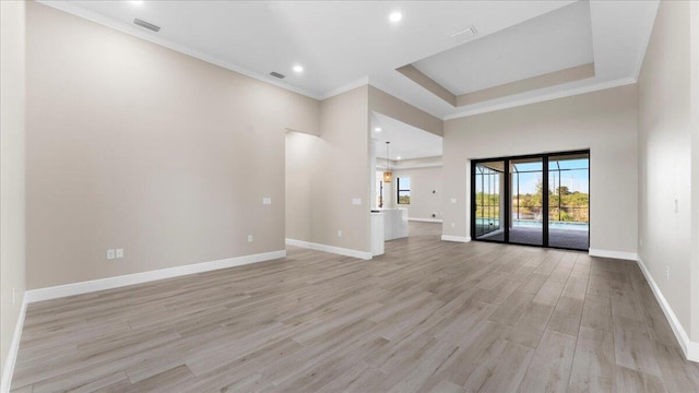 unfurnished living room with crown molding, a raised ceiling, and light wood-type flooring