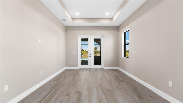 empty room with french doors, light hardwood / wood-style floors, and a raised ceiling