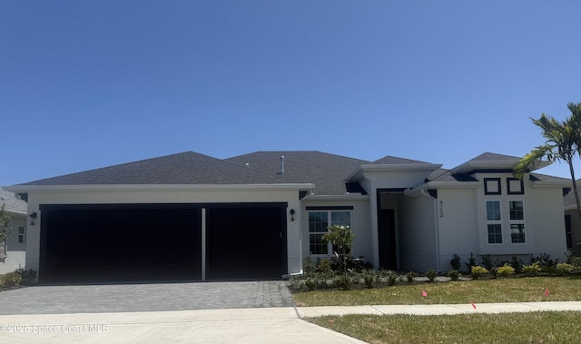 prairie-style home featuring decorative driveway, an attached garage, and stucco siding