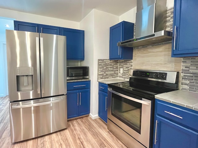 kitchen with backsplash, stainless steel appliances, light hardwood / wood-style floors, and wall chimney exhaust hood