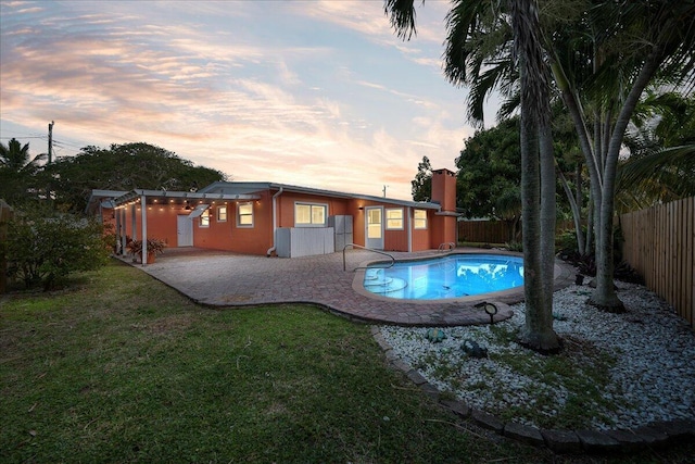 pool at dusk featuring a patio and a yard