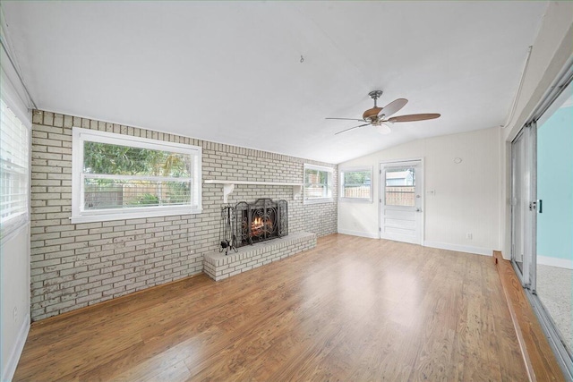 unfurnished living room with ceiling fan, a fireplace, brick wall, vaulted ceiling, and plenty of natural light