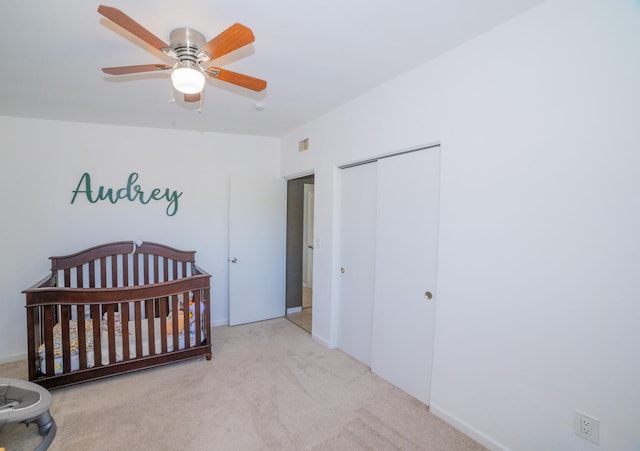 bedroom featuring a closet, light carpet, a nursery area, and ceiling fan