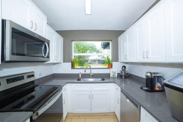 kitchen with sink, light tile floors, white cabinets, appliances with stainless steel finishes, and backsplash