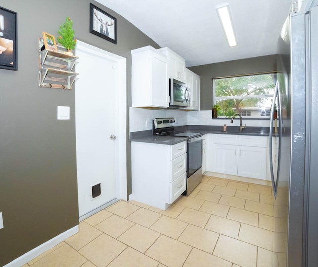 kitchen featuring sink, stainless steel appliances, light tile floors, white cabinets, and vaulted ceiling