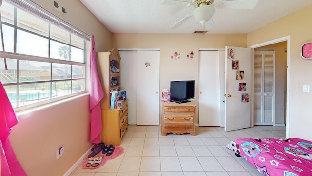 bedroom featuring light tile floors, a textured ceiling, ceiling fan, and two closets