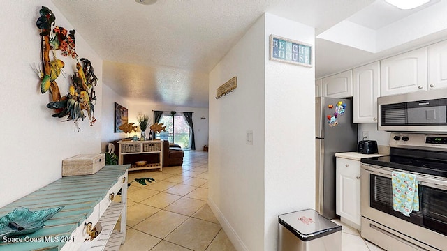 kitchen featuring white cabinets, light tile flooring, a textured ceiling, and stainless steel appliances