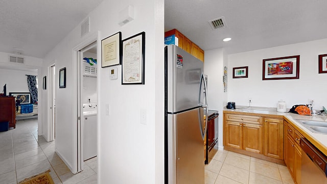 kitchen with stainless steel appliances, washer / clothes dryer, sink, and light tile floors