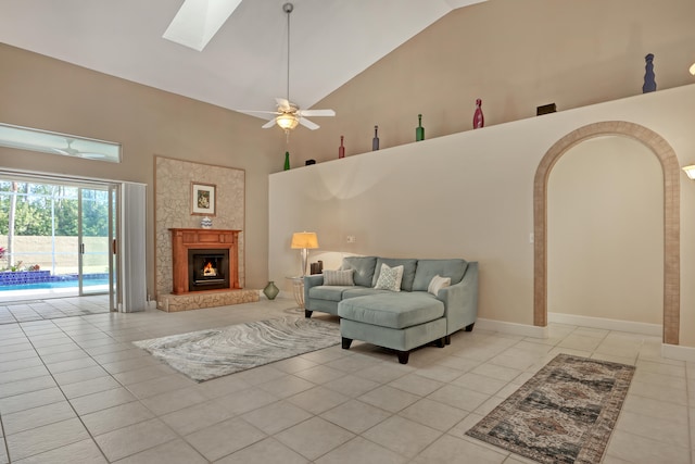 living room featuring a skylight, ceiling fan, light tile floors, and high vaulted ceiling