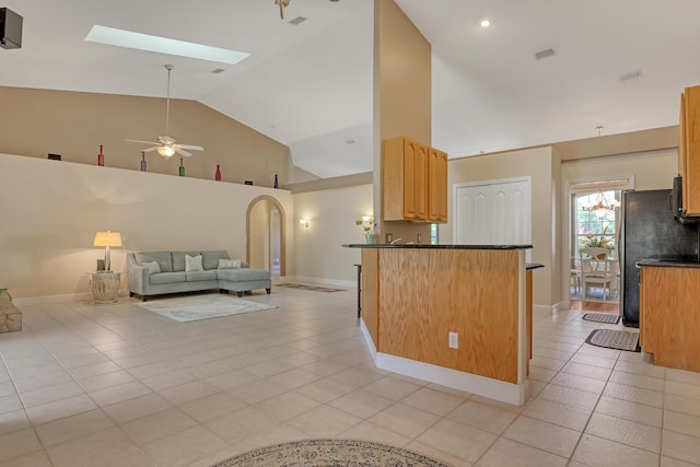 kitchen featuring a skylight, decorative light fixtures, ceiling fan, high vaulted ceiling, and light tile floors