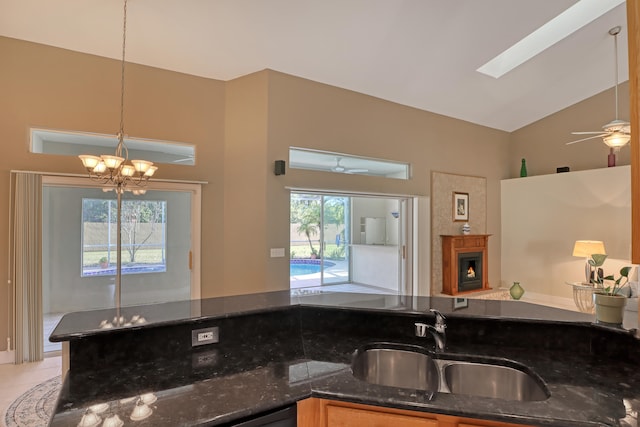 kitchen featuring pendant lighting, dark stone counters, a skylight, ceiling fan with notable chandelier, and sink