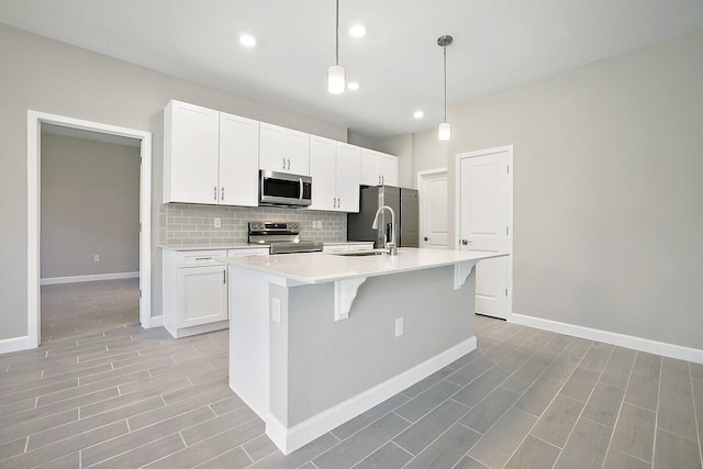 kitchen featuring tasteful backsplash, stainless steel appliances, a kitchen island with sink, pendant lighting, and white cabinets