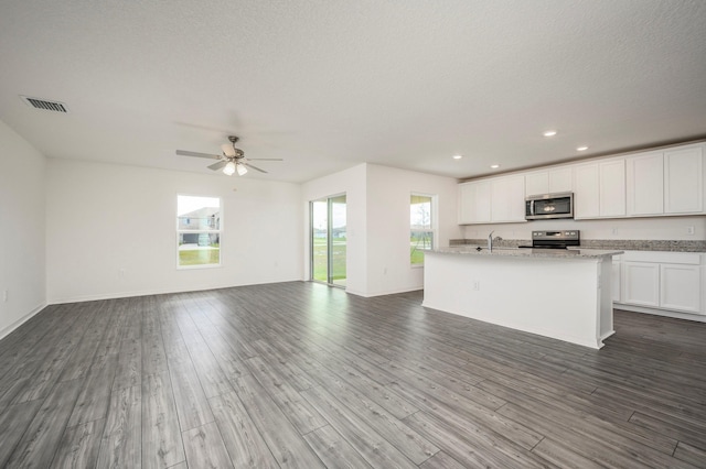 kitchen featuring an island with sink, stainless steel appliances, white cabinets, and dark wood-type flooring