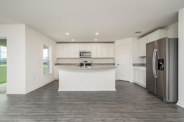 kitchen with stainless steel appliances, light stone countertops, a center island with sink, white cabinets, and dark hardwood / wood-style flooring