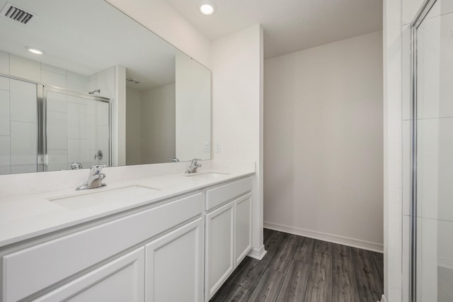 bathroom with a shower with shower door, double vanity, and wood-type flooring