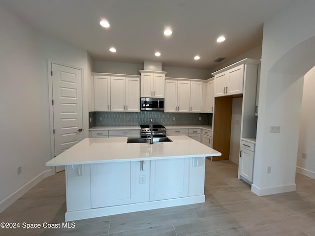 kitchen featuring an island with sink, sink, and white cabinetry