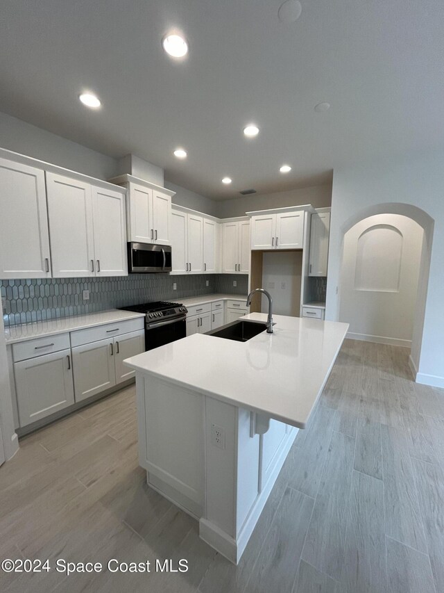 8526 Lyside Dr, Melbourne, FL 32940 - kitchen featuring arched walkways, decorative backsplash, stainless steel appliances, a sink, and a center island with sink