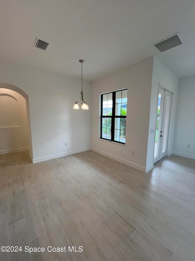 unfurnished room with an inviting chandelier and light hardwood / wood-style flooring