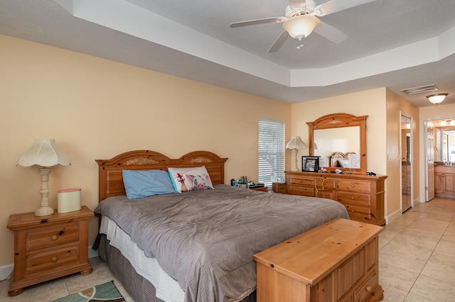 bedroom with a raised ceiling, ensuite bath, ceiling fan, and light tile floors