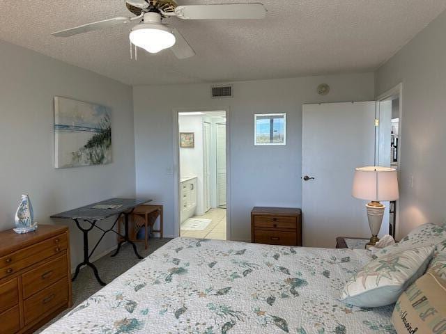 bedroom featuring a textured ceiling, carpet flooring, ensuite bathroom, and ceiling fan