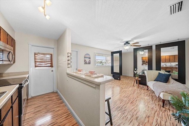 kitchen featuring ceiling fan, a textured ceiling, kitchen peninsula, appliances with stainless steel finishes, and light wood-type flooring