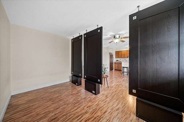 interior space with a textured ceiling, ceiling fan, and light wood-type flooring