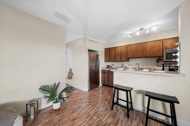 kitchen featuring kitchen peninsula, stainless steel appliances, dark wood-type flooring, a kitchen bar, and a textured ceiling