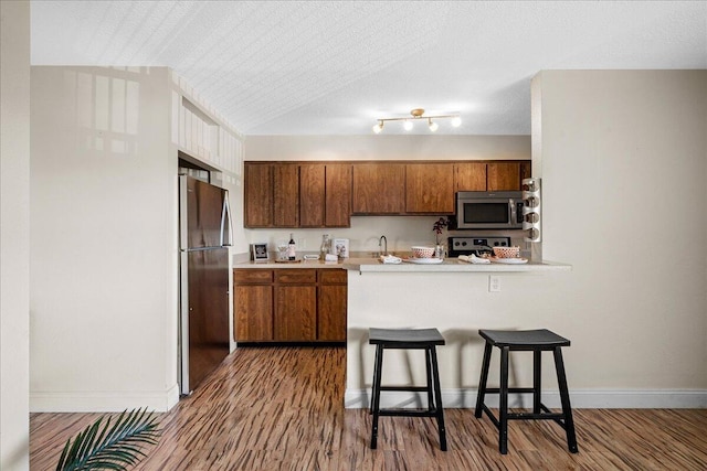 kitchen featuring stainless steel appliances, a kitchen bar, rail lighting, a textured ceiling, and dark hardwood / wood-style floors