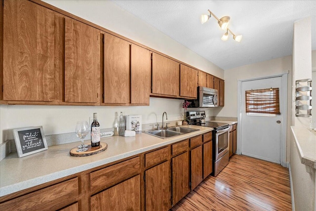 kitchen with light hardwood / wood-style floors, stainless steel appliances, a textured ceiling, and sink